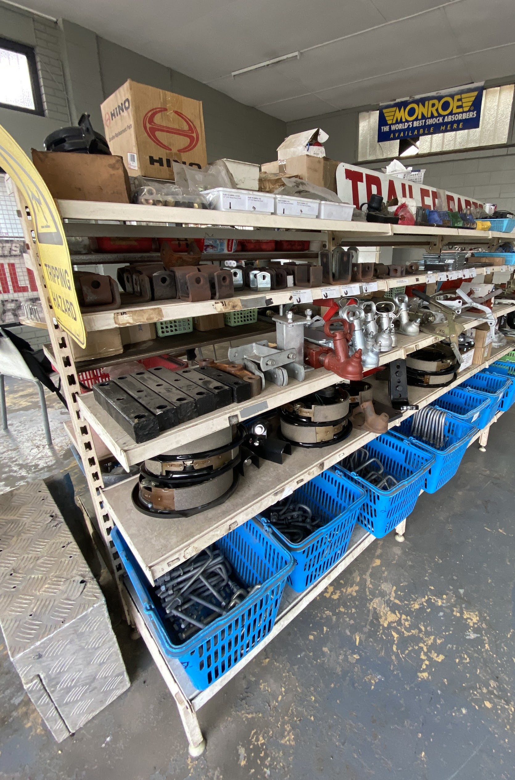Shelves of trailer parts inside the Geben Mechanical workshop, with a vehicle on the hoist behind